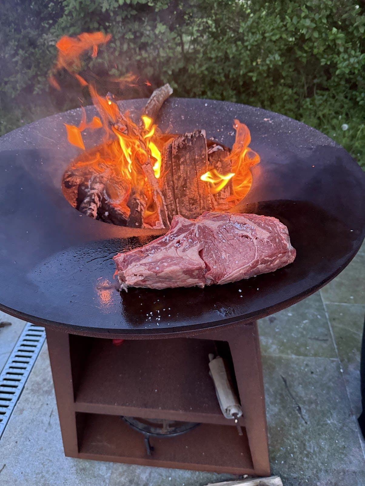 Die Feuerschale auf der Terrasse mit Holzfeuer, ein Rinderkotelett auf der Plancha